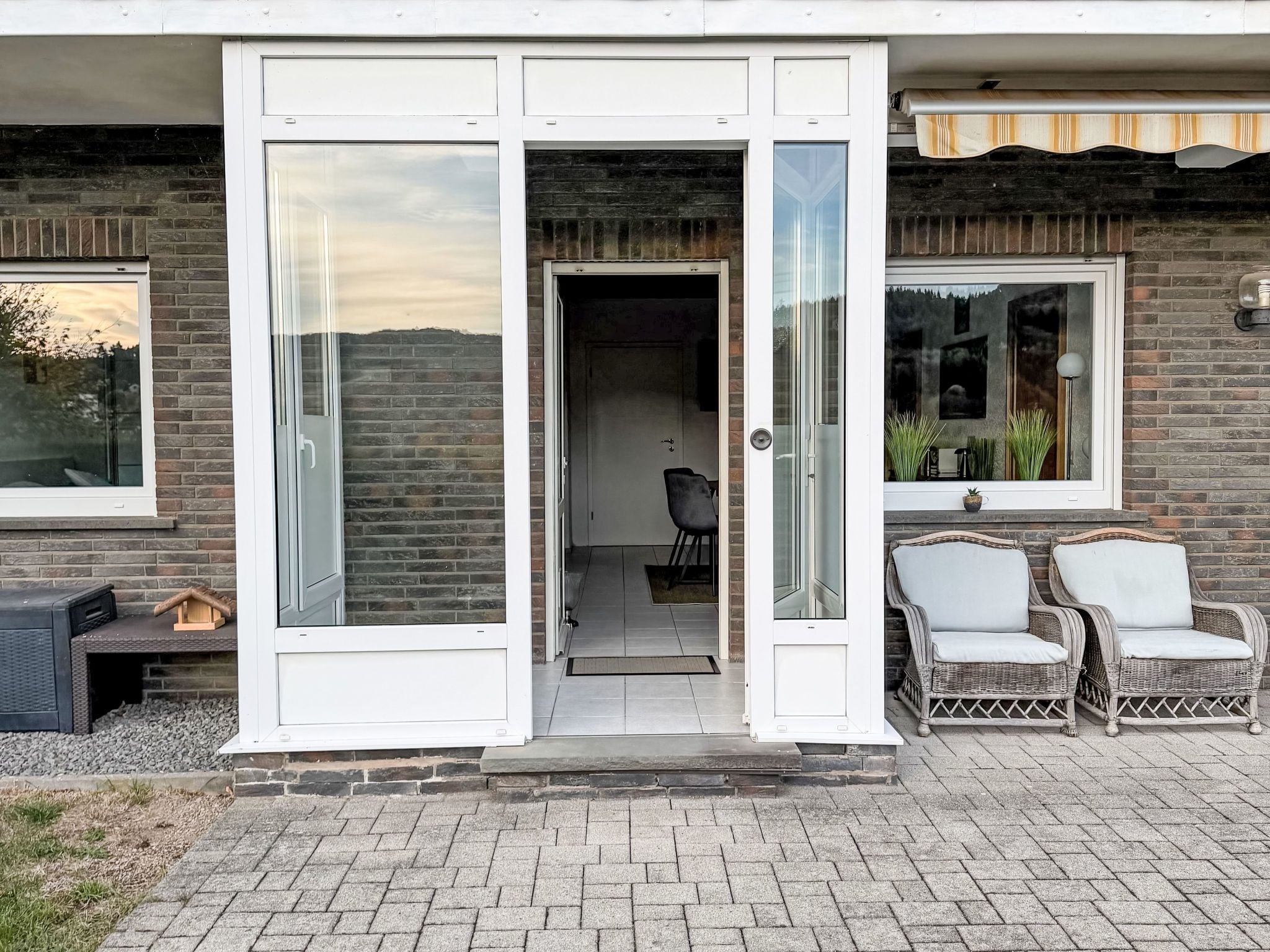 Ein modernes Haus mit Glastür, Ziegelaußenwand und zwei Korbstühlen vor der Tür.