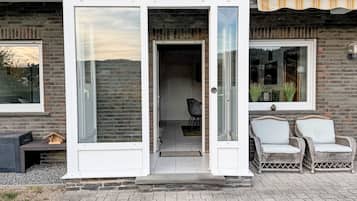 Una casa moderna con puerta de cristal, fachada de ladrillo y dos sillas de mimbre en el exterior.