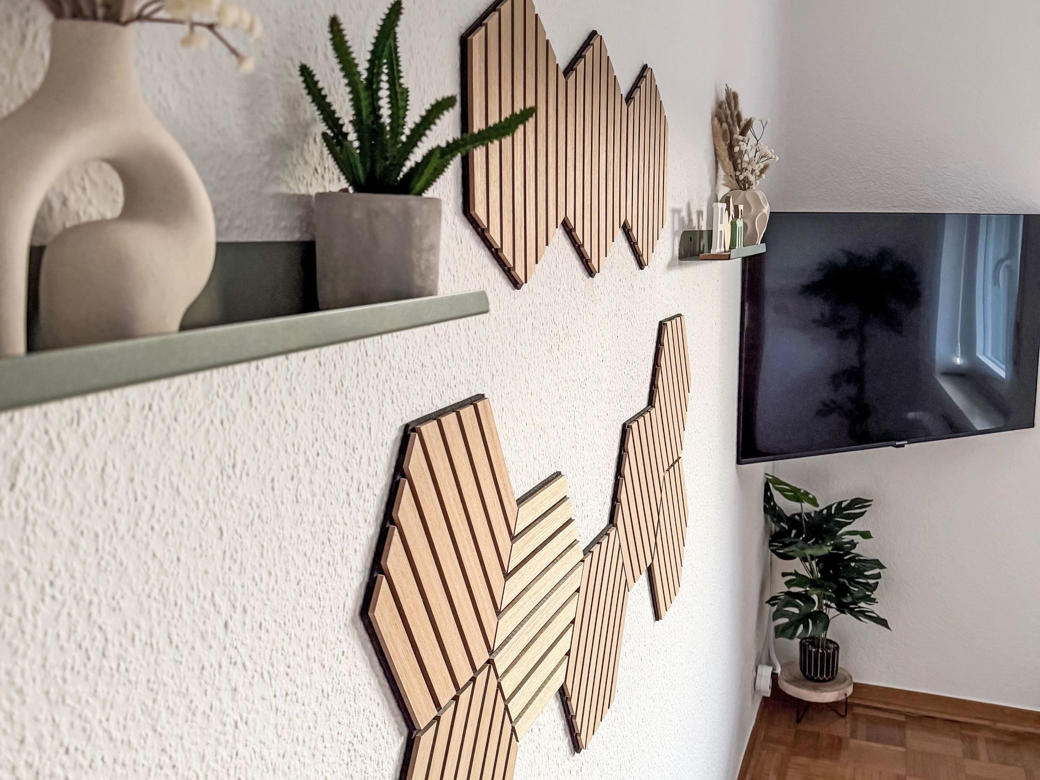 Ein modernes Wohnzimmer mit einem großen Flachbildfernseher an der Wand, dekorativer Holzbildkunst, einer Zimmerpflanze und einem kleinen Tisch mit einer Vase.