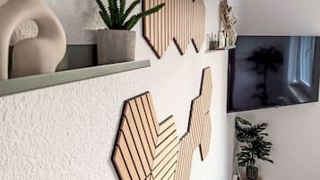 Una sala de estar moderna con un televisor de pantalla plana grande montado en la pared, decoración de madera en la pared, una planta en maceta y una pequeña mesa con un florero.