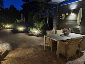 An outdoor patio area with a table and chairs, surrounded by plants and decorative lighting. - Holiday Home With 2 Bedrooms (Nieuwvliet)