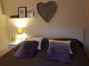 A neatly made bed with two fluffy pillows, a bedside lamp, and a heart-shaped wall decoration. - Holiday Home With 2 Bedrooms (Nieuwvliet)