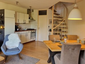 A modern kitchen with white cabinets, a stove, and a dining area with a wooden table and chairs. - Holiday Home With 2 Bedrooms (Nieuwvliet)