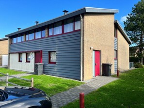 A two-story building with a red door and windows with white curtains. - Wijk de Brabander 58 (Cadzand-Bad)