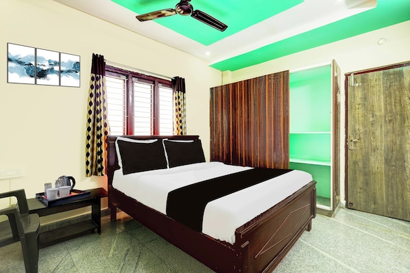 Una habitación de hotel con cama, escritorio con hervidor y ventana con cortinas.