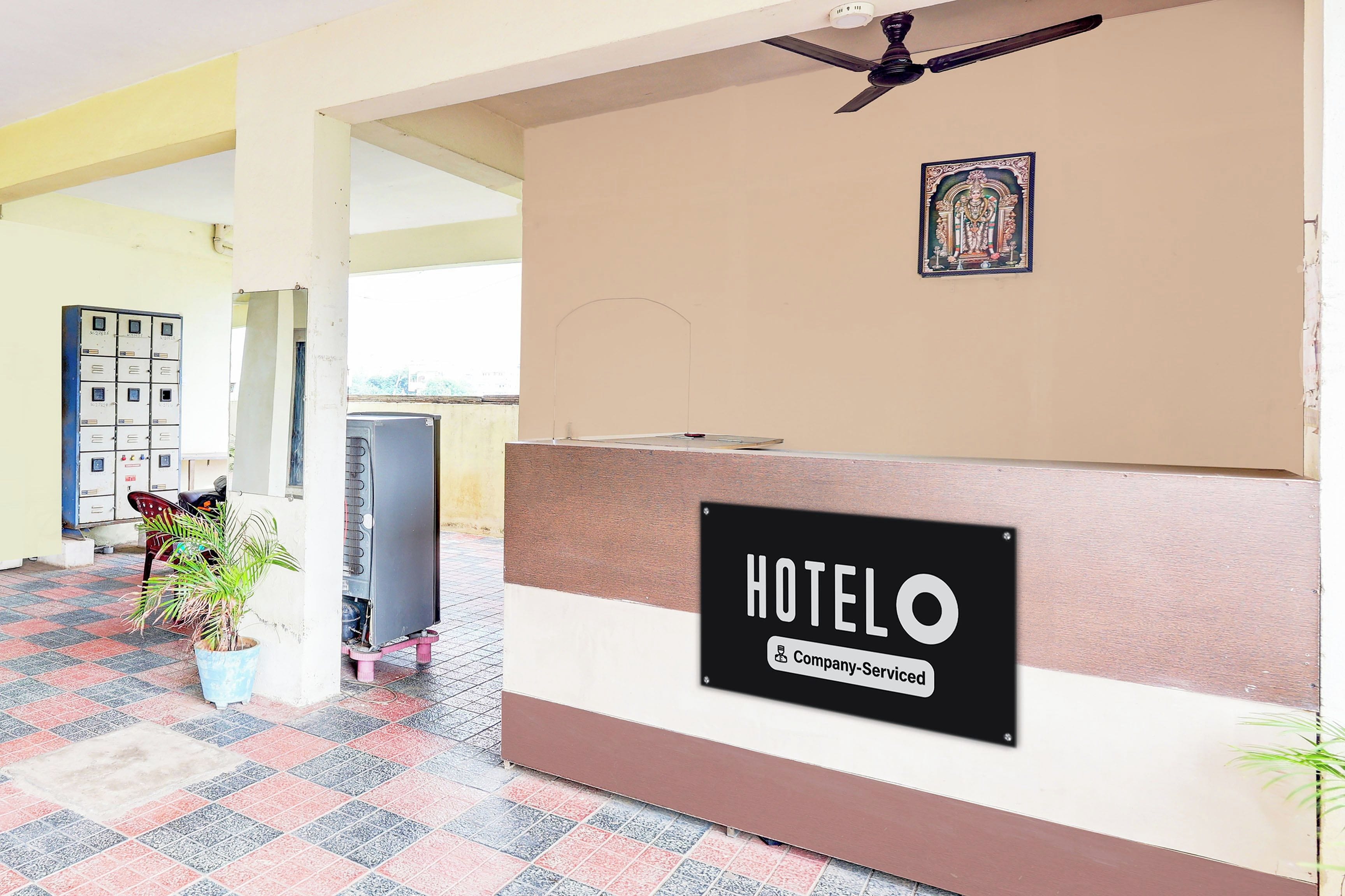 A hotel reception area with a sign indicating company-serviced rooms, a ceiling fan, a potted plant, and a wall-mounted decorative item.