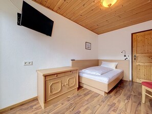 Ein Schlafzimmer mit einem Bett, einem Holzschrank, einem an der Wand montierten Fernseher und einer Holzbalkendecke.