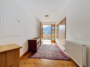 A hallway with a wooden cabinet, a patterned rug, and a view of a wooden deck and mountains through an open door. - Gästehaus Kurz by Interhome (Fliess/Landeck/Tirol West)