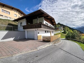 Une maison à deux étages avec un balcon, une allée et une vue sur la montagne.