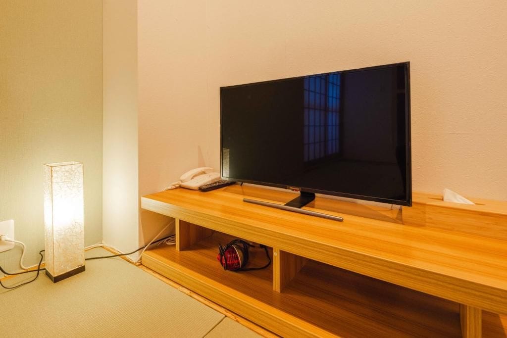 A television on a wooden stand with a remote control and a phone beside it.