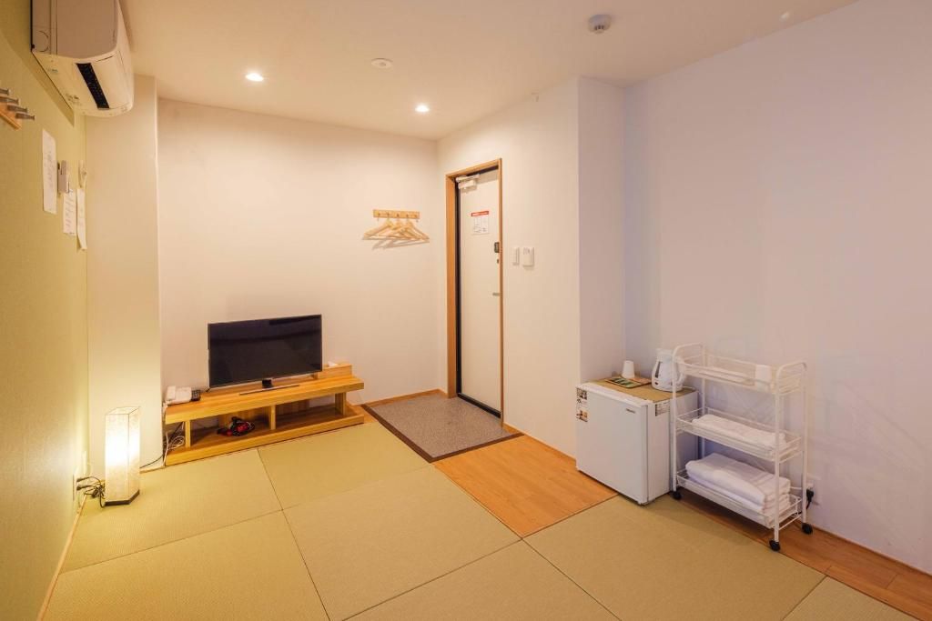 Una habitación con una televisión sobre un mueble de madera, un armario blanco pequeño, una estantería blanca y una puerta con un perchero.
