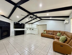 Een ruime woonkamer met een open haard, een flatscreen televisie, een bank en een keukenhoek.