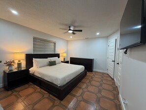 A bedroom with a bed, nightstands, a ceiling fan, a TV, and a patterned floor. - Spacious 4BR Retreat on 2 Acres •Sleeps 9 (San Benito)