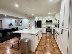 A modern kitchen with white cabinets, a central island, and a dining area with chairs. - Spacious 4BR Retreat on 2 Acres •Sleeps 9 (San Benito)