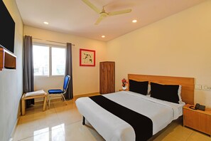 A hotel room with a bed, a desk, a chair, a nightstand, a telephone, and a ceiling fan. - Super Collection O ECIL Crossway (Hyderabad)