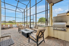 Eine überdachte Terrasse mit Gartenmöbeln, einem Grill und Blick auf einen Golfplatz.