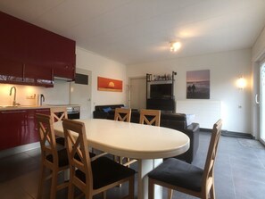 A modern kitchen with red cabinets, a dining table with chairs, a sofa, and a fireplace. - Wielewaal Side Wing (Cadzand-Bad)