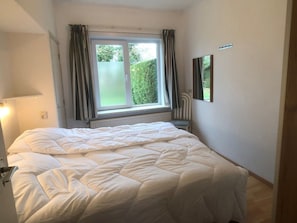 A bedroom with a bed, a window with curtains, a chair, and a mirror on the wall. - Wielewaal Side Wing (Cadzand-Bad)