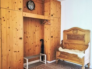 A wooden room with a bed, a coat rack, a clock, and a hanging coat. - Dein Bergmoment by Interhome (Wildhaus)