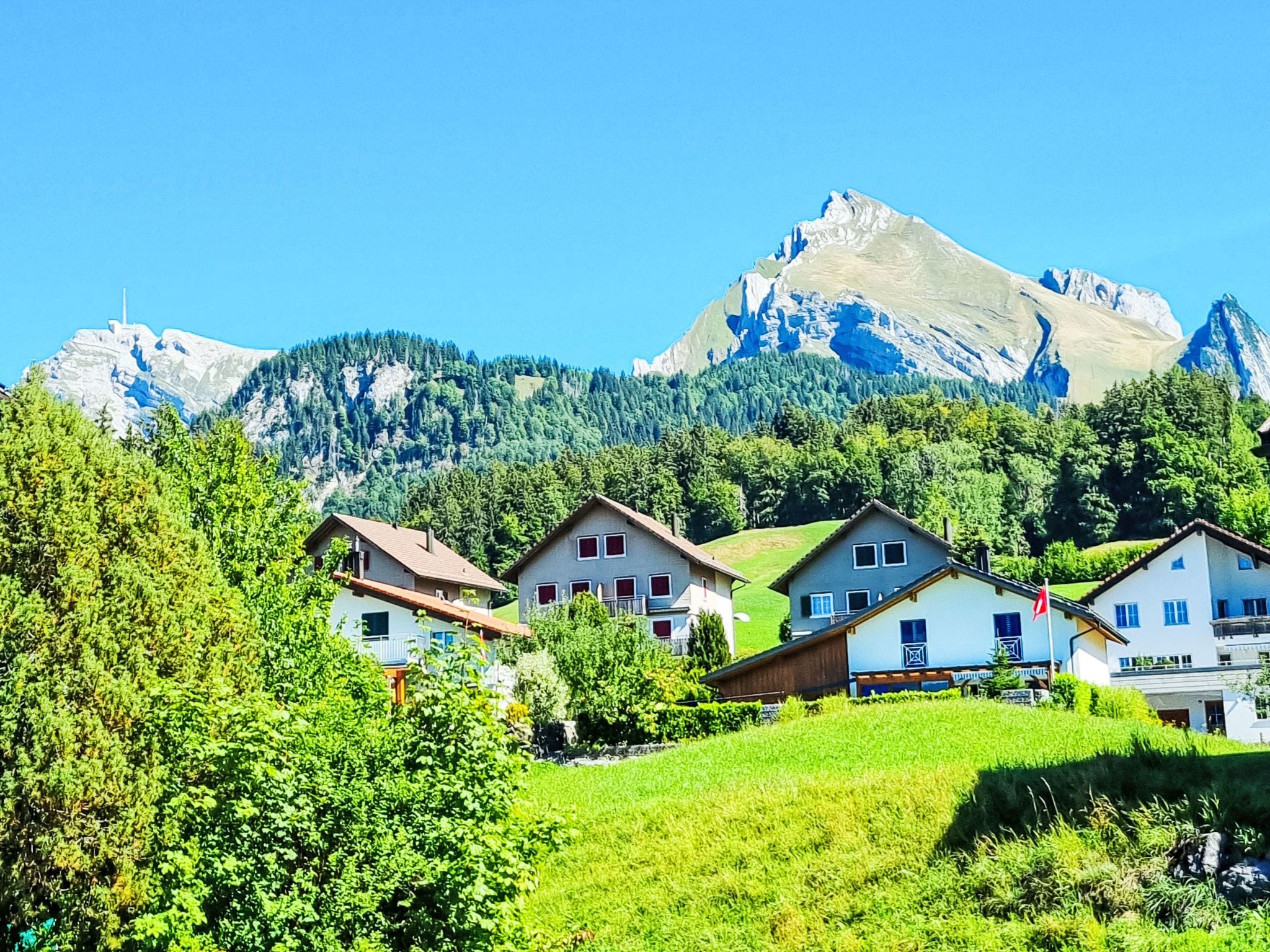A mountain village with traditional houses, a clear sky, and a prominent mountain peak in the background.