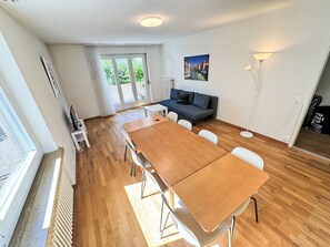 A modern living room with a wooden dining table, a sofa, and a large window. - Apartment  by Interhome (Zurich)