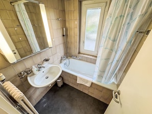 A bathroom with a sink, mirror, shower, and window. - Apartment  by Interhome (Zurich)