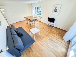 A modern living room with a sofa, a coffee table, a TV stand, and a dining area with chairs and a table. - Apartment  by Interhome (Zurich)