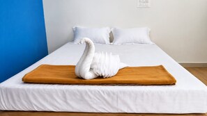 A bed with white bedding and a brown blanket, a white swan decoration, and a blue wall. - The Coastal Sunset (Gokarna)