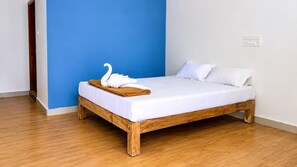 A single bed with a wooden frame, white bedding, and a swan-shaped towel on the side. - The Coastal Sunset (Gokarna)