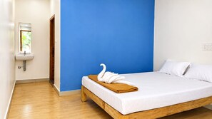 A bedroom with a wooden bed, white bedding, a blue accent wall, a white sink, and a window with a view. - The Coastal Sunset (Gokarna)