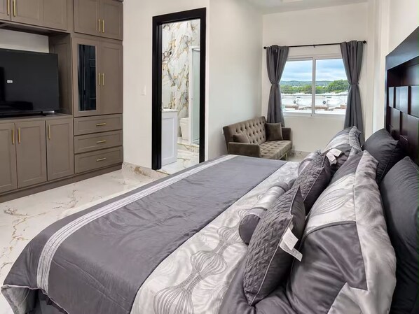 A bedroom with a bed, a television, a sofa, and a window with curtains.