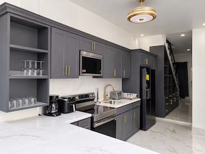 A modern kitchen with grey cabinets, a stainless steel microwave, a coffee maker, and a black refrigerator.