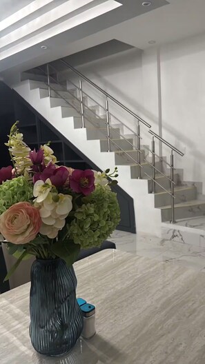 A modern interior with a staircase, a vase of flowers, and a trash bin.