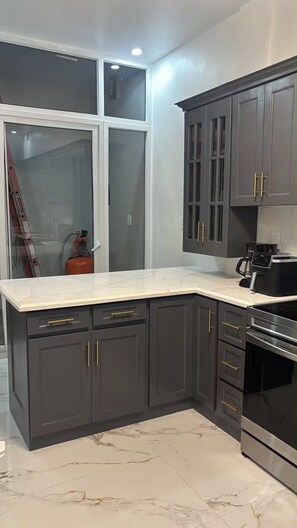 A modern kitchen with dark grey cabinets, a white marble countertop, and stainless steel appliances. - Twin Paradise Villas II (Hato Nuevo)