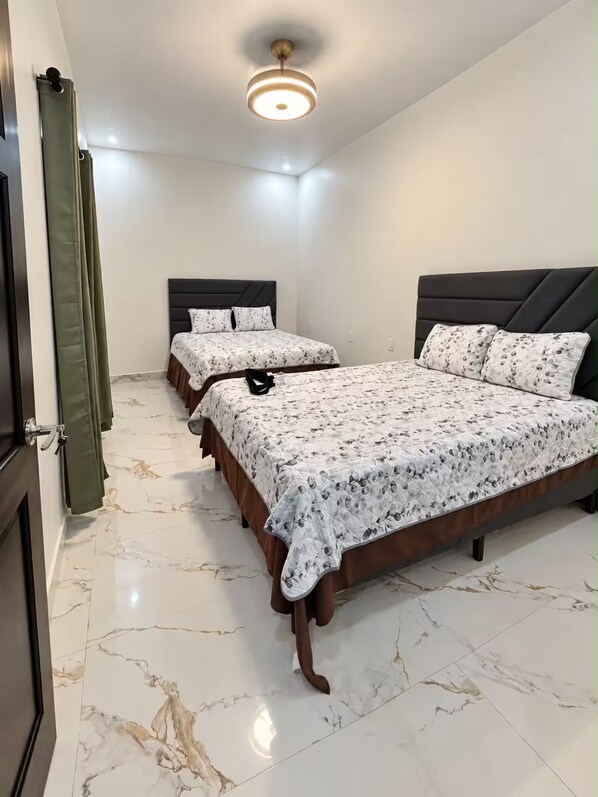 A bedroom with two beds, a ceiling light, and a door with a green curtain.