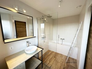 Ein modernes Badezimmer mit einem Holzwaschtisch, einem großen Spiegel, einer gläsernen Duschkabine und einer Badewanne.