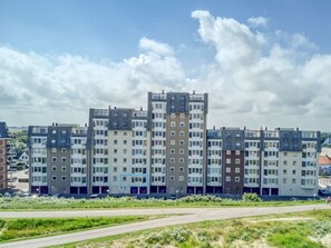 Ein mehrgeschossiges Wohngebäude mit moderner Architektur, das eine Kombination aus flachen und geneigten Dächern sowie eine Reihe von Balkonen zeigt.