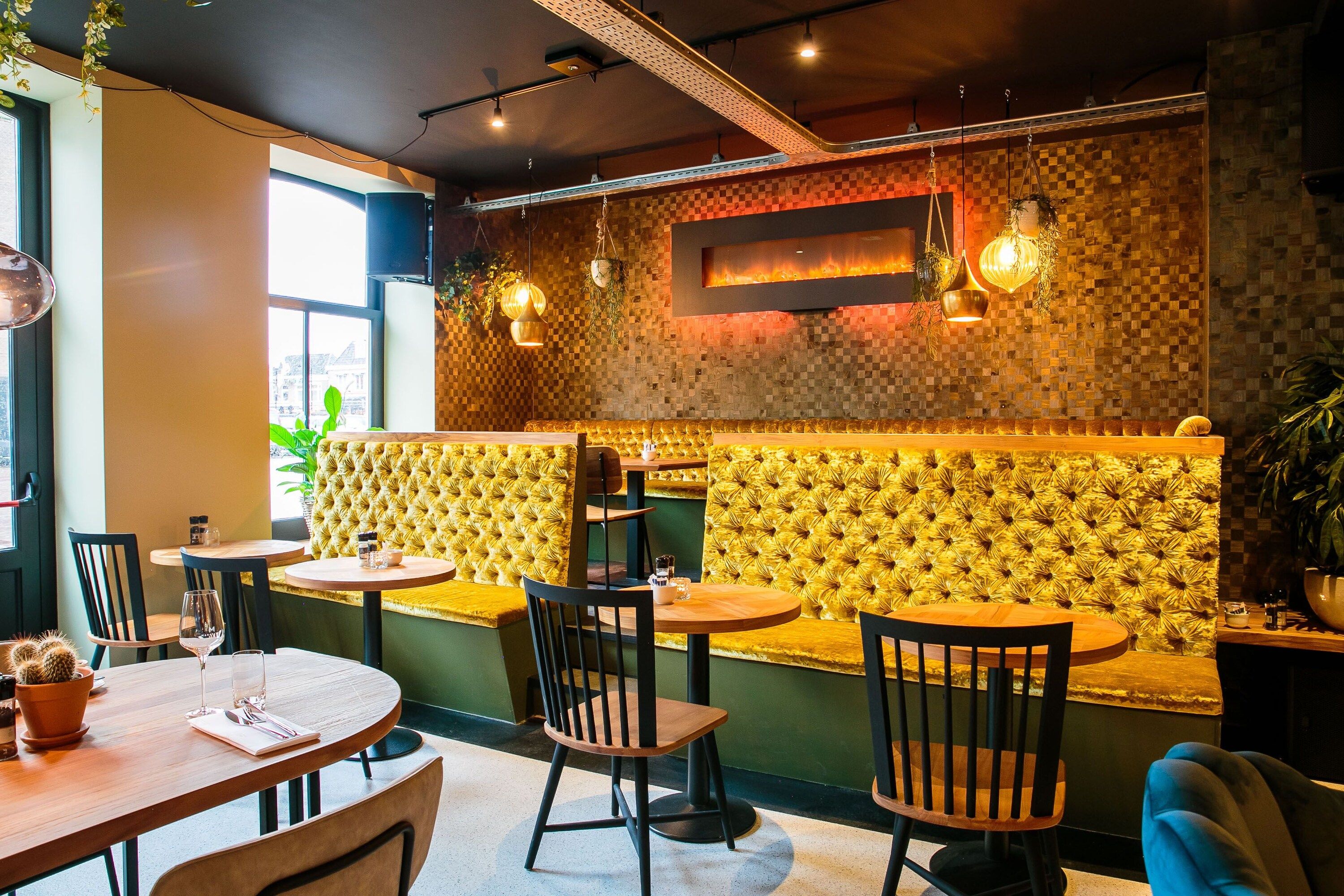 A restaurant interior with round tables, cushioned booths, hanging pendant lights, and a checkered wall design.