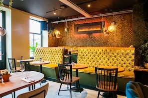 A restaurant interior with round tables, cushioned booths, hanging pendant lights, and a checkered wall design.