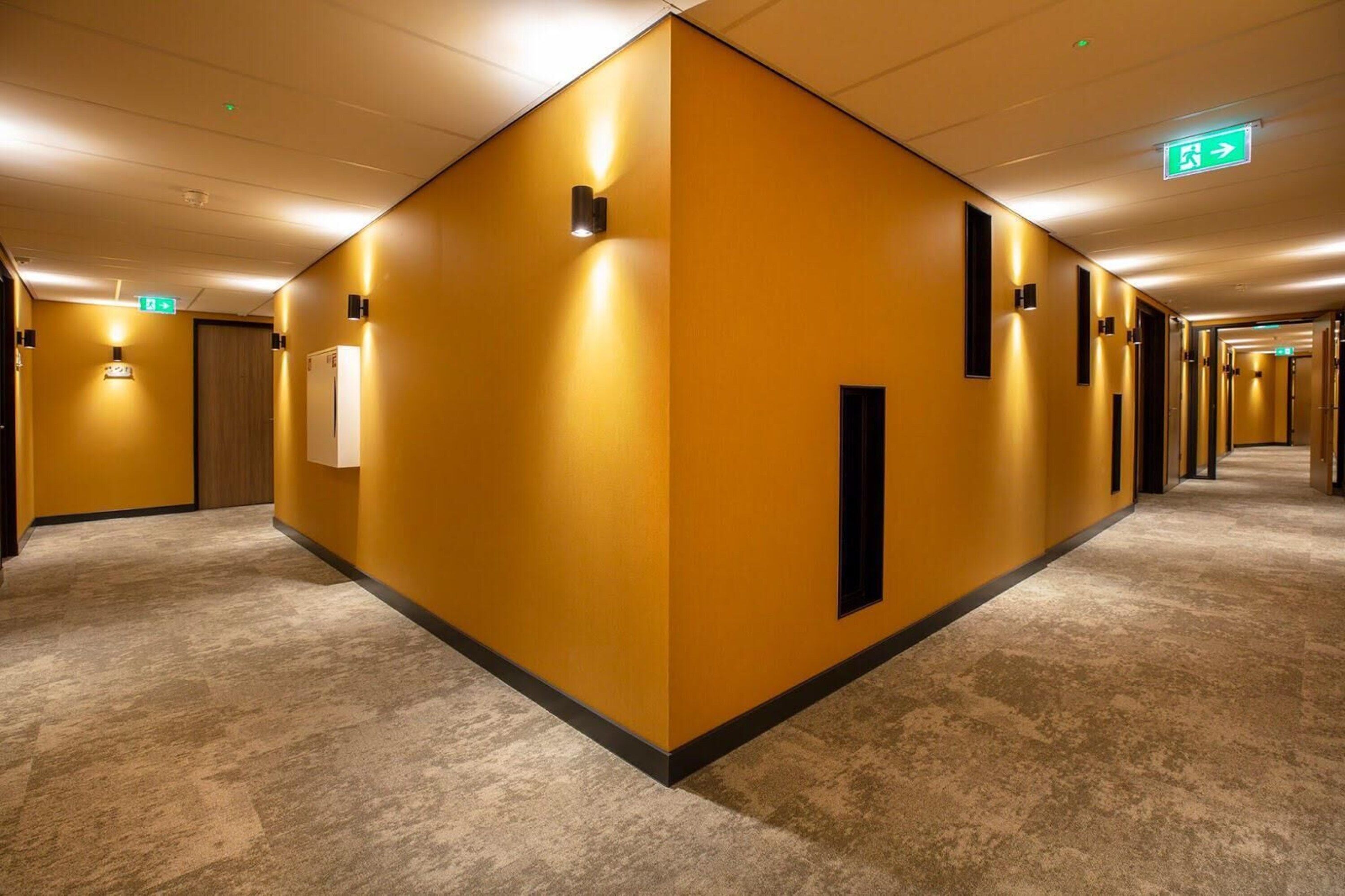 Ein Hotelgang mit einheitlich gelben Wänden, Teppichboden und mehreren Türen.