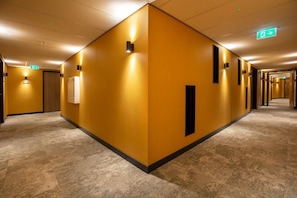 Un couloir d’hôtel avec un mur jaune uniforme, un sol recouvert de moquette et de nombreuses portes.