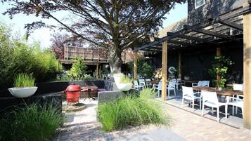 An outdoor patio with a barbecue grill, white chairs, and a pergola structure.