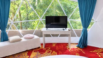 Ein Zimmer mit einem großen Fenster, einem weißen Sofa mit Kissen, einem kleinen Tisch mit Fernseher und einem gemusterten Teppich.