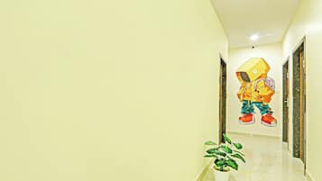 A hallway with a potted plant, a wall-mounted artwork of a cartoon character, and a door on the right.