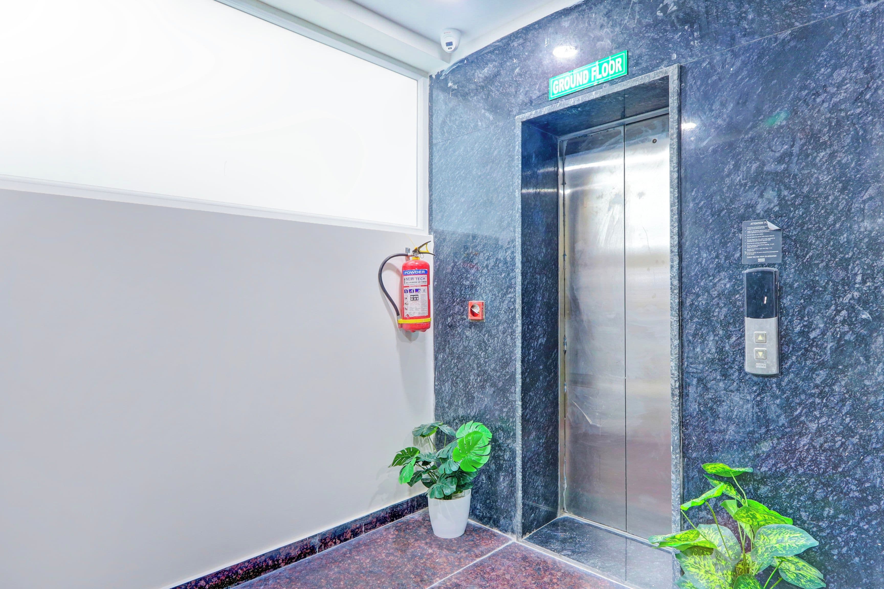 An elevator with a 'Ground Floor' sign above it, a fire extinguisher mounted on the wall, and a potted plant at the base.