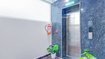 An elevator with a 'Ground Floor' sign above it, a fire extinguisher mounted on the wall, and a potted plant at the base.