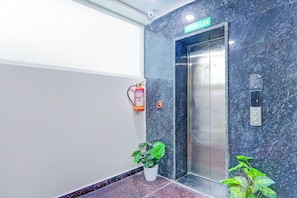 An elevator with a 'Ground Floor' sign above it, a fire extinguisher mounted on the wall, and a potted plant at the base.