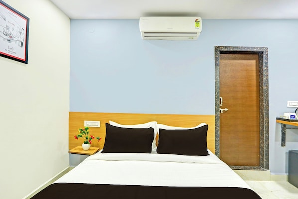 A hotel room with a bed, a nightstand, a wall-mounted air conditioner, and a door.