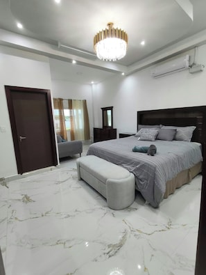 A bedroom with a large bed, a bench, a mirror, and a chandelier. - Twin Paradise Villas I (Hato Nuevo)