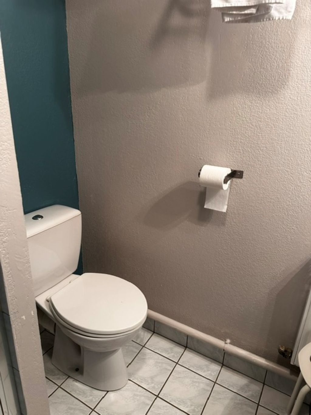 Un baño pequeño con inodoro, dispensador de toallas y soporte para papel higiénico en la pared.